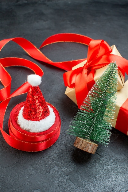 Vista frontale di bellissimi regali con nastro rosso e cappello di Babbo Natale albero di Natale su un tavolo scuro