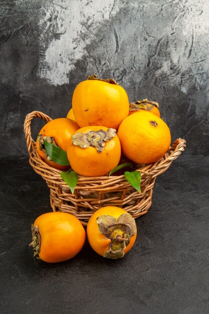 Vista frontale di cachi dolci freschi all'interno del cesto su foto a colori di frutta da tavola scura