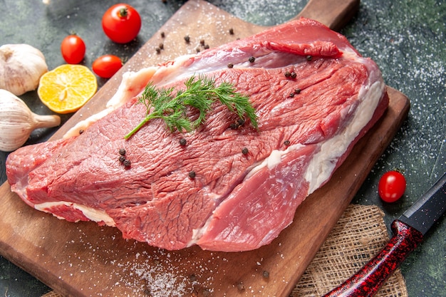 Vista frontale di carne rossa cruda fresca su tagliere di legno su asciugamano color nudo aglio limone su sfondo di colore misto