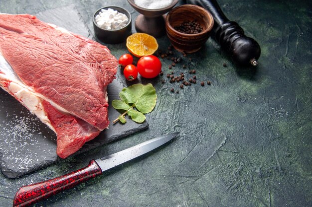 Vista frontale di carne rossa cruda fresca su vassoio nero pepe sale limone coltello a martello in legno su sfondo di colore scuro