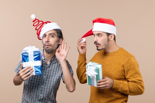 Vista frontale di due ragazzi interessati che indossano cappelli di Babbo Natale e tengono regali