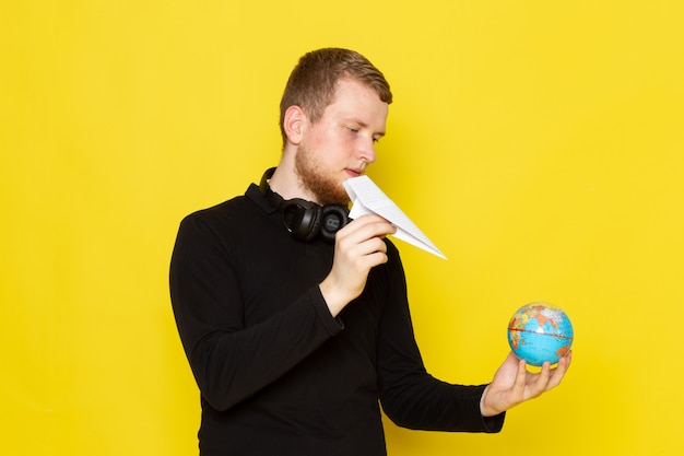 Vista frontale di giovane maschio in camicia nera che tiene aereo di carta e piccolo globo