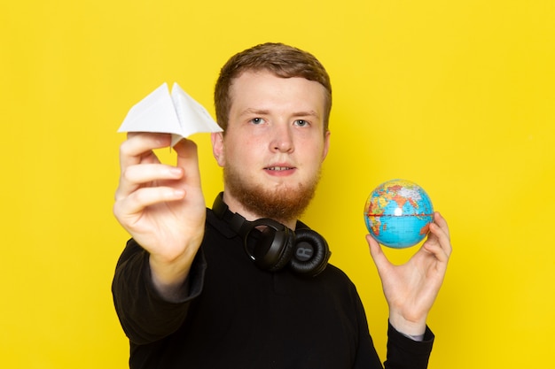 Vista frontale di giovane maschio in camicia nera che tiene aereo di carta e piccolo globo