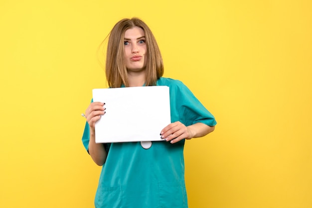 Vista frontale di giovane medico femminile che tiene file sulla parete gialla