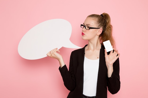 Vista frontale di impiegato femminile in giacca rigorosa nera con cartello bianco e carta sulla parete rosa