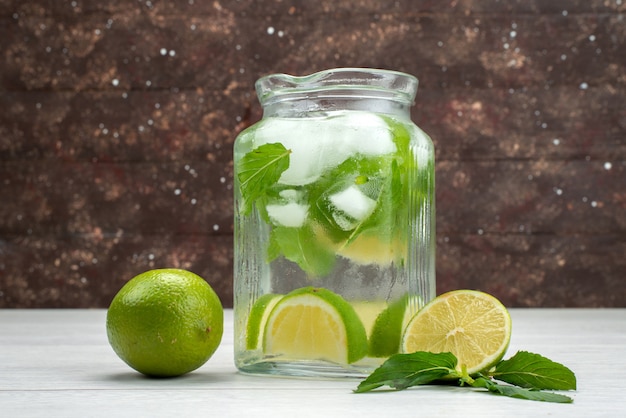 Vista frontale di lime fresche all'interno e all'esterno di un barattolo di vetro su succo tropicale di agrumi grigio e frutta