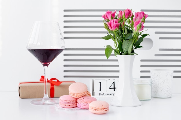 Vista frontale di macarons con bicchiere di vino e vaso di rose