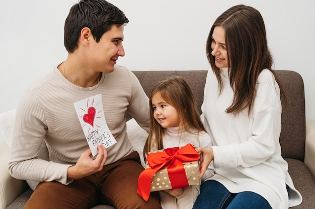 Vista frontale di mamma e papà con la figlia e il regalo a casa