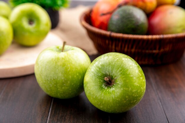 Vista frontale di mele verdi con un secchio di frutta come pera mango su una superficie di legno