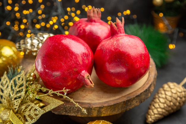 Vista frontale di melograni freschi intorno ai giocattoli di natale su sfondo scuro foto a colori frutta natalizia