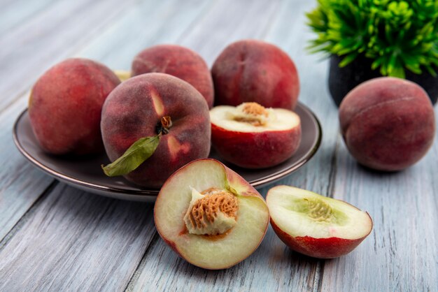 Vista frontale di mezze pesche deliziose dolci fresche su un piatto su superficie di legno grigia