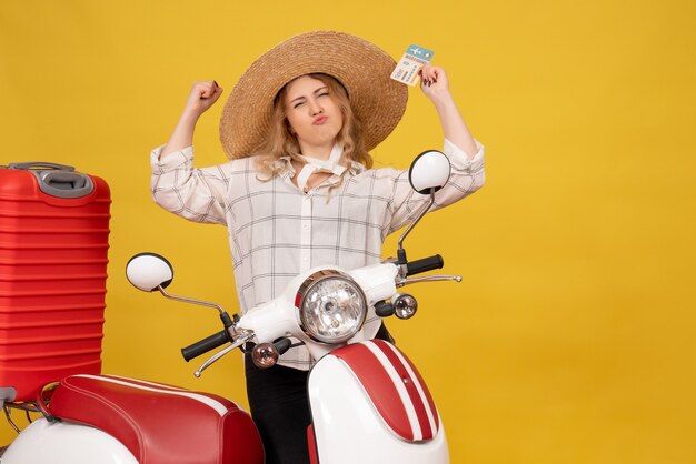 Vista frontale di orgogliosa giovane donna che indossa un cappello raccogliendo i suoi bagagli seduto sulla moto e mostrando il biglietto