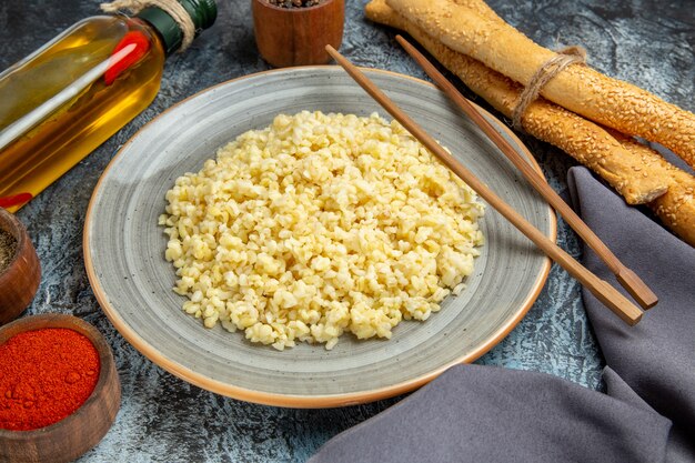 Vista frontale di orzo perlato cotto con condimenti su superficie chiara