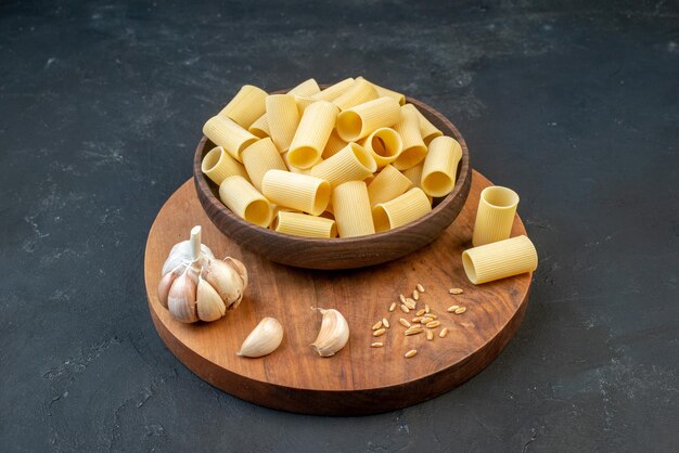 Vista frontale di pasta cruda in una ciotola marrone garlics riso su tavola di legno rotonda su sfondo nero