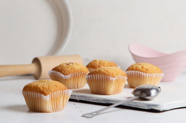 Vista frontale di piccole torte squisite con zucchero in polvere all'interno del piatto con cucchiaio sulla superficie bianca