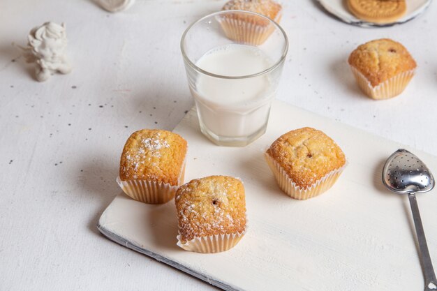 Vista frontale di piccoli dolci squisiti con zucchero in polvere e bicchiere di latte sulla superficie bianca