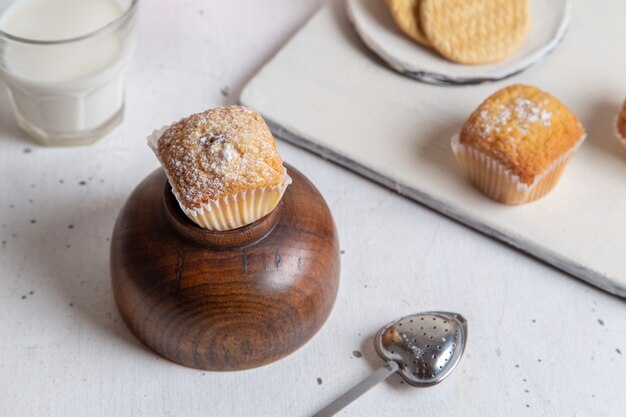 Vista frontale di piccoli dolci squisiti con zucchero in polvere e bicchiere di latte sulla superficie bianca