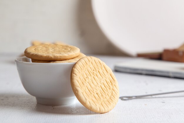 Vista frontale di piccoli dolci squisiti con zucchero in polvere e biscotti rotondi sulla superficie bianca