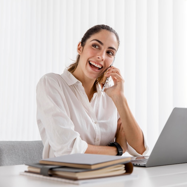 Vista frontale di smiley imprenditrice lavorando con smartphone e laptop