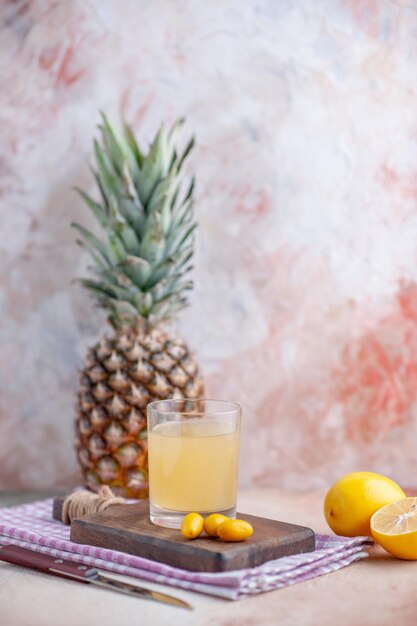 Vista frontale di succo di frutta e kumquat su tagliere di legno su asciugamano viola spogliato limoni e pompelmi tagliati interi su sfondo colori pastello