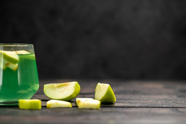 Vista frontale di un delizioso succo in un bicchiere e una mela tritata su sfondo scuro