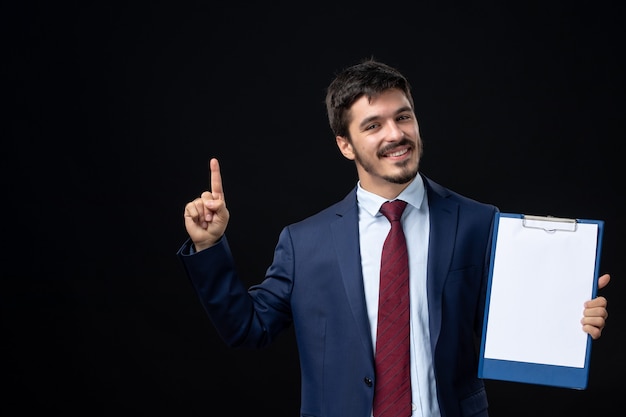 Vista frontale di un giovane adulto soddisfatto in tuta che tiene spazio libero per scrivere e puntare verso l'alto su un muro scuro isolato