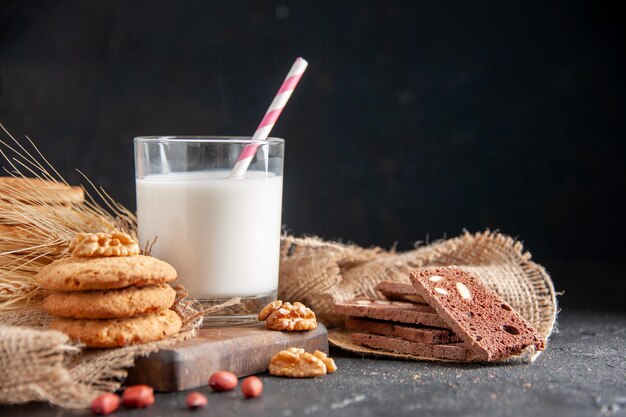 Vista frontale di un latte fresco in un bicchiere di biscotti picchi su arachidi di noci di asciugamano di colore nudo su superficie scura