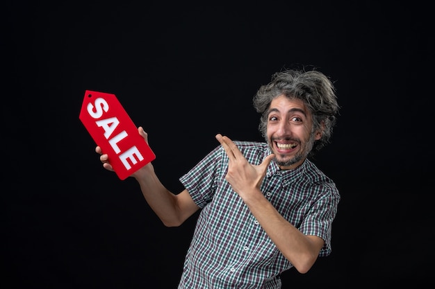 Vista frontale di un uomo molto eccitato che tiene in mano il cartello di vendita rosso sul muro scuro
