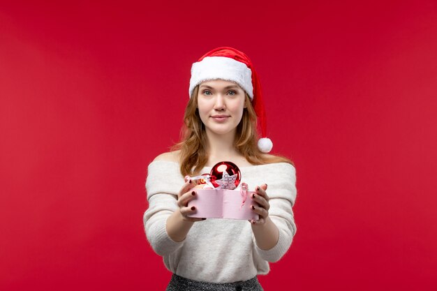 Vista frontale di una giovane donna che tiene in mano i giocattoli di natale sul pavimento rosso per le vacanze di natale rosso