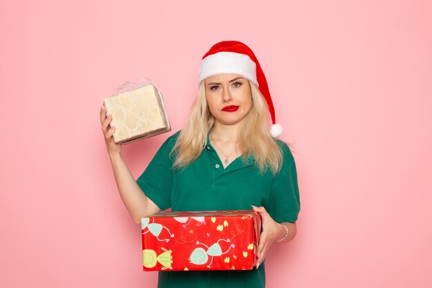 Vista frontale di una giovane donna con regali di Natale sulla parete rosa