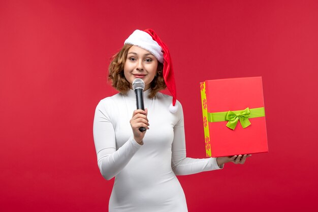 Vista frontale di una giovane donna con regalo e microfono su rosso