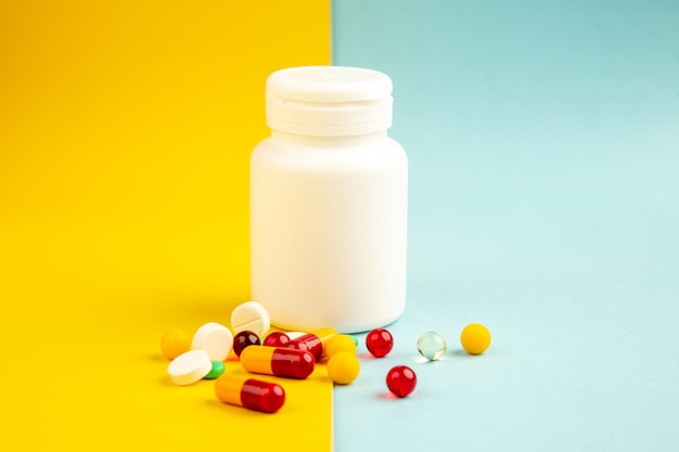 Vista frontale diverse pillole con pallone di plastica su sfondo giallo-blu laboratorio sanitario scienza ospedale virus covid- farmaco a colori pandemico