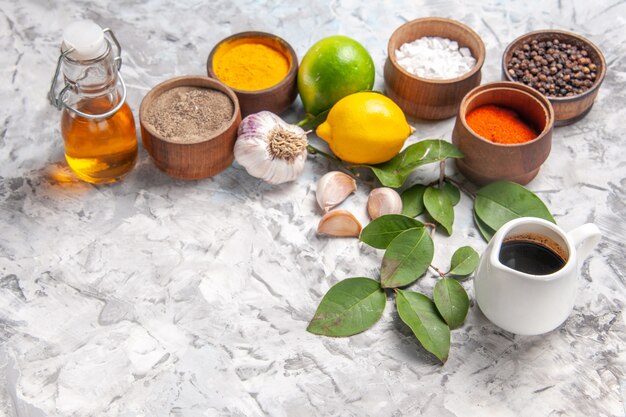 Vista frontale diversi condimenti con limone e aglio su olio da pavimento bianco sale piccante di frutta