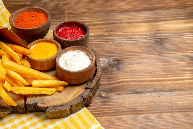 Vista frontale diversi condimenti con patatine fritte su tavola di legno marrone pasto veloce con patate