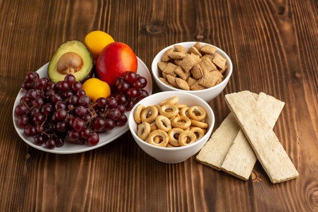 Vista frontale diversi frutti con cracker e biscotti sullo scrittorio di legno marrone