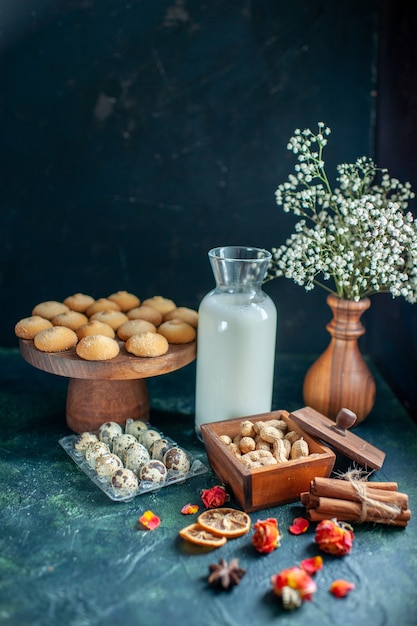 Vista frontale dolci deliziosi biscotti con latte e noci sulla superficie blu scuro