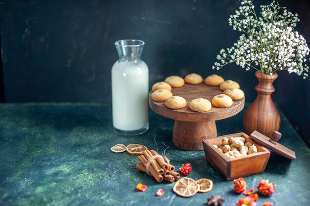 Vista frontale dolci deliziosi biscotti con latte e noci sulla superficie blu scuro