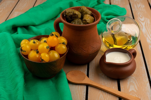 vista frontale dolma verde farina di carne tritata all'interno della pentola marrone con yogurt giallo pomodori e olio d'oliva sul rustico marrone