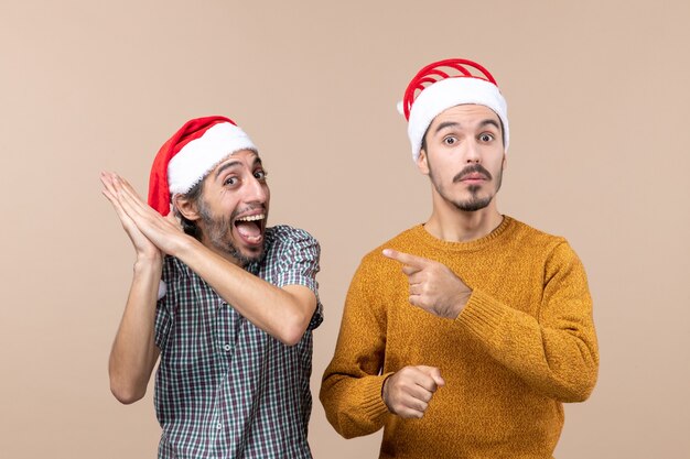 Vista frontale due ragazzi con cappelli di Babbo Natale un dito punto che mostra quello felice su sfondo beige isolato