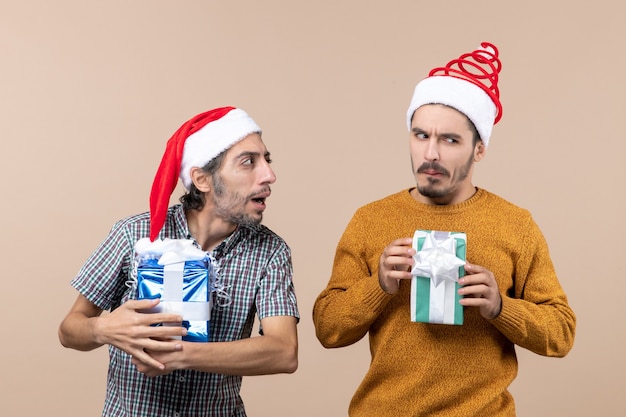 Vista frontale due ragazzi confusi che indossano cappelli della Santa e che tengono i regali su fondo isolato beige