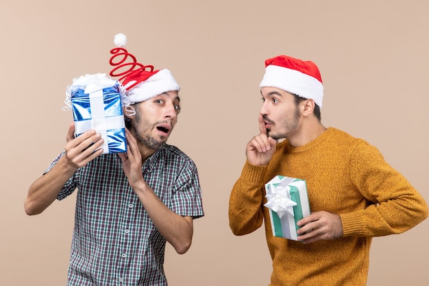 Vista frontale due ragazzi confusi uno controllando i suoi regali di Natale e l'altro facendo segno shh su sfondo beige isolato