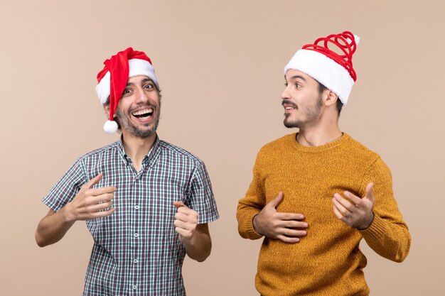 Vista frontale due ragazzi felici con cappelli di Babbo Natale che ridono su sfondo beige isolato