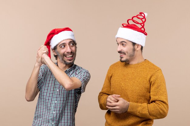 Vista frontale due ragazzi sorridenti con cappelli di Babbo Natale guardando a vicenda su sfondo beige isolato