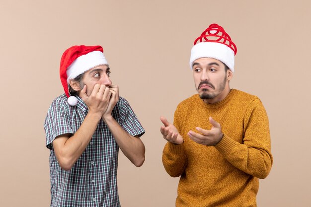 Vista frontale due ragazzi stupiti con cappelli di Babbo Natale su sfondo beige isolato