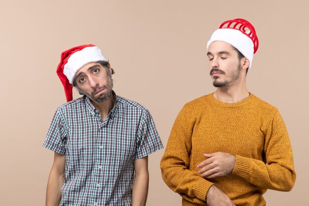 Vista frontale due ragazzi un depresso e un assonnato con cappelli di Babbo Natale su sfondo beige isolato