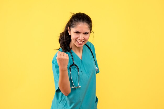 Vista frontale felicissima giovane dottoressa in uniforme in piedi su sfondo giallo