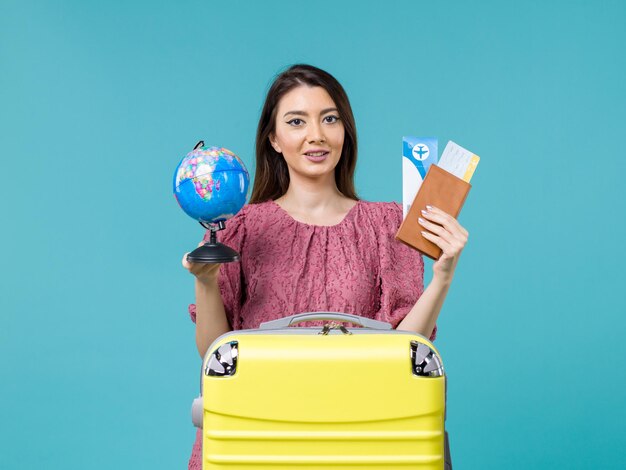 Vista frontale femminile in viaggio tenendo i biglietti e globo su sfondo blu donna viaggio viaggio mare viaggio viaggio