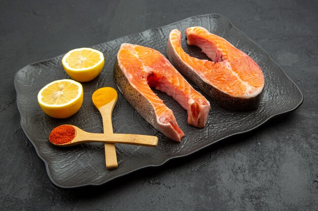 Vista frontale fette di carne fresca all'interno del piatto con fette di limone su sfondo scuro piatto cibo farina di pesce foto costola animale