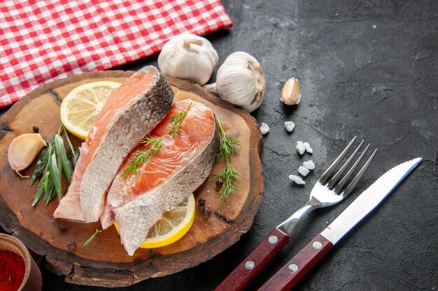 Vista frontale fette di pesce fresco con fette di limone aglio e condimenti su carne scura piatto di pesce colore cibo foto crudo