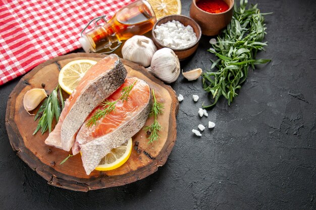 Vista frontale fette di pesce fresco con fette di limone aglio e condimenti su pesce scuro colore piatto carne foto crudo